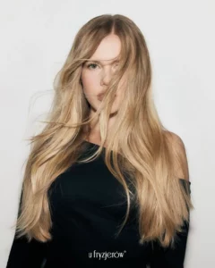 Kobieta z długimi, prostymi blond włosami, naturalna stylizacja z lekko rozwianymi pasmami fryzjer warszawa